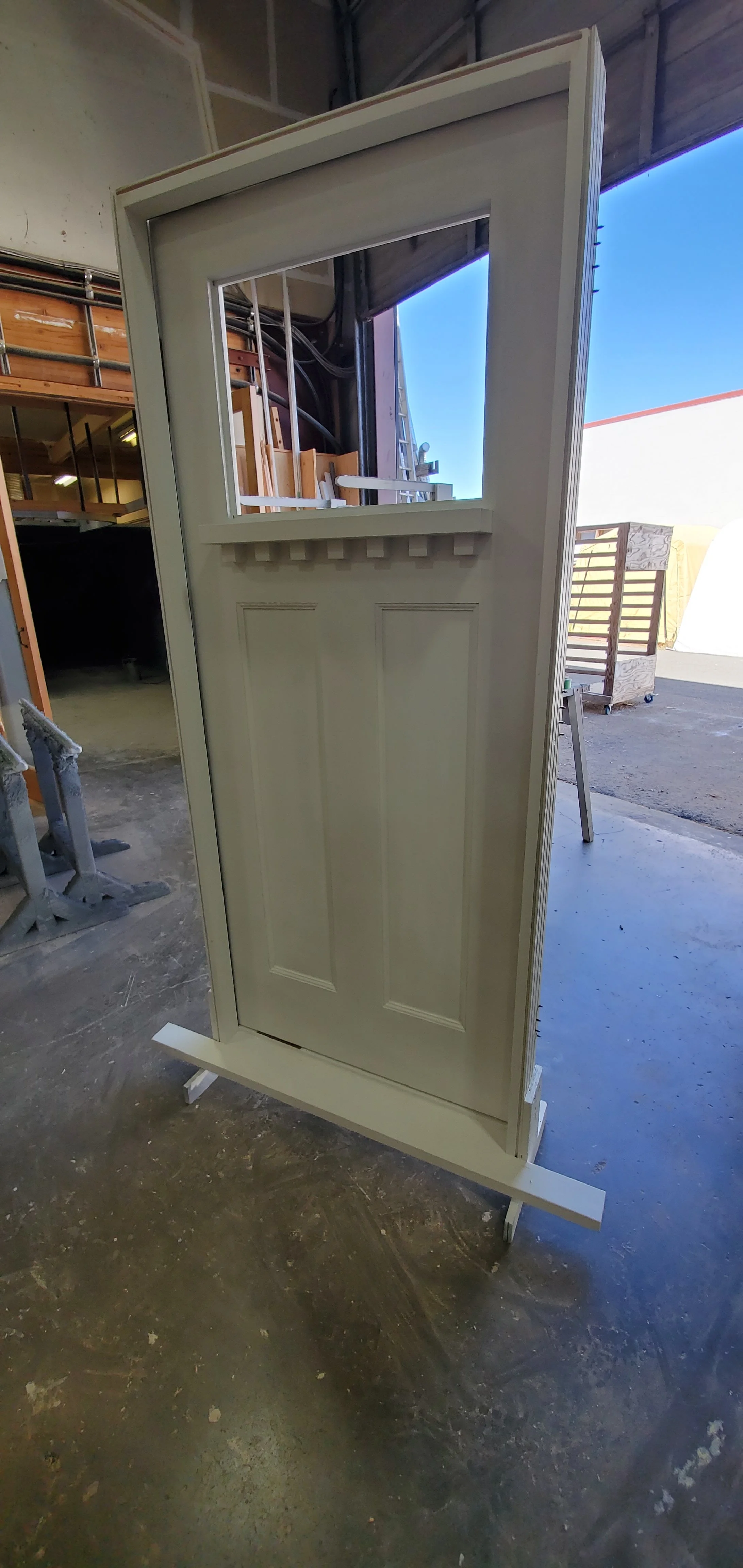 A white door with a window at the top, displayed on a stand in a workshop.