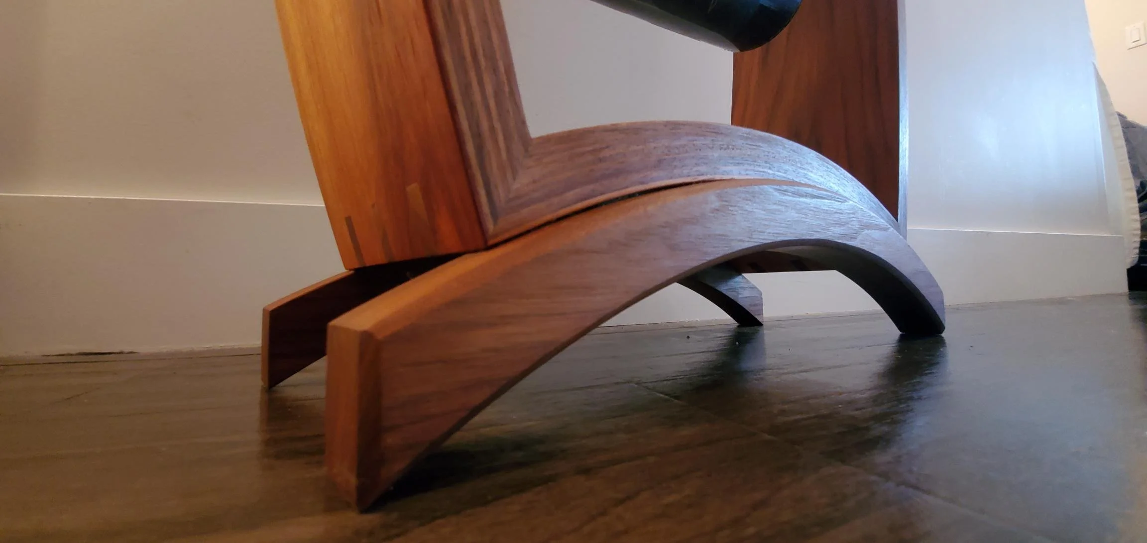 Close-up of a wooden chair leg with a curved design, showing the wood grain and floor underneath.