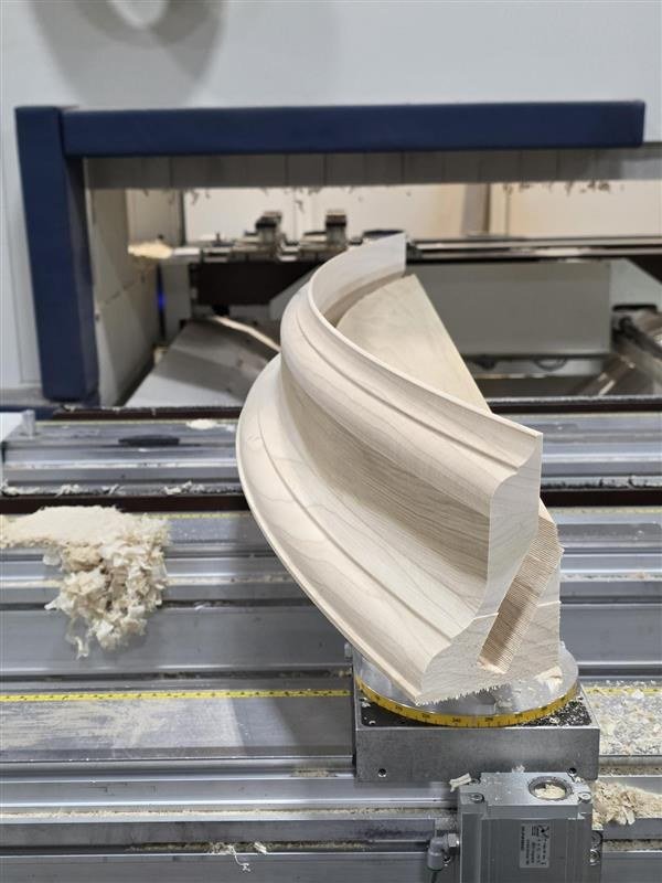 Woodworking CNC machine carving detailed curved design in a piece of wood.
