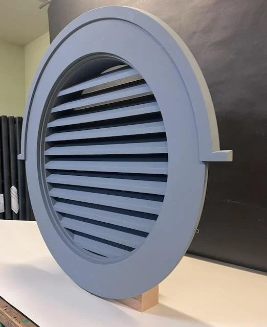 A gray circular air vent with horizontal slats, mounted on a stand.