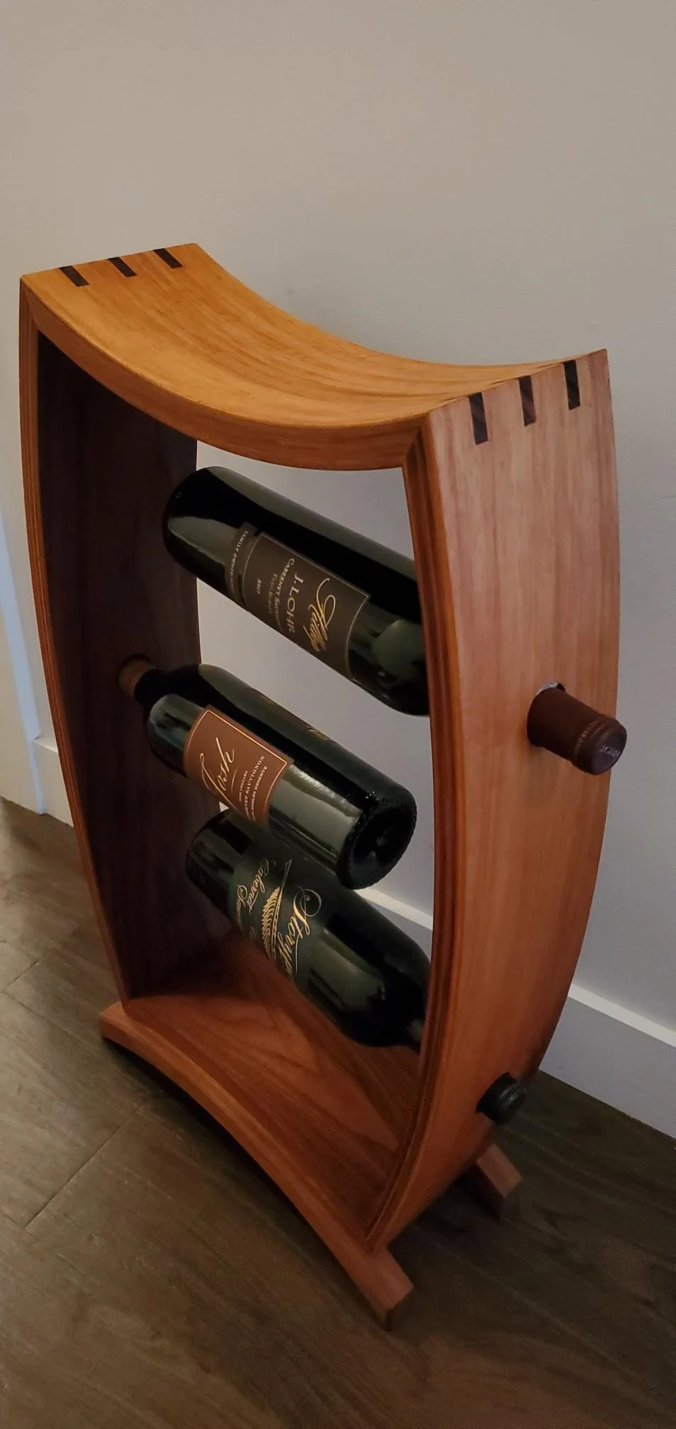 A wooden wine bottle rack with three bottles of wine stored horizontally inside.