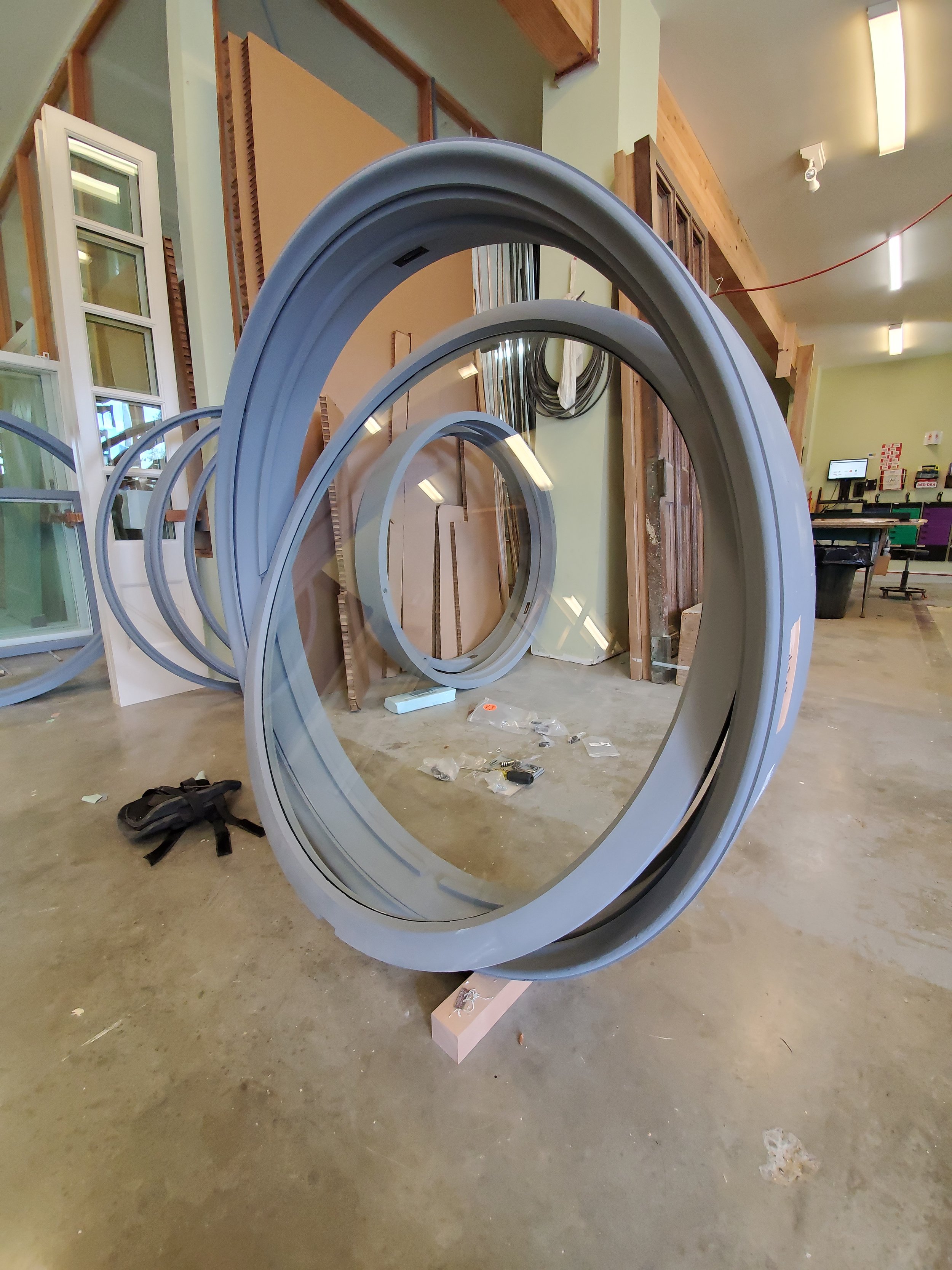 Large metal donut-shaped rings stacked on a stand in a workshop or construction space with tools and building materials around.