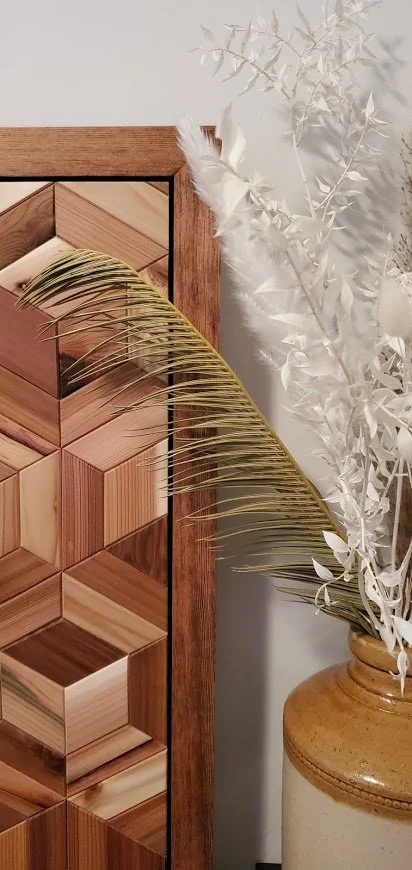 Decorative wooden cabinet with geometric patterns next to a brown vase containing white and beige dried foliage and palm leaves.