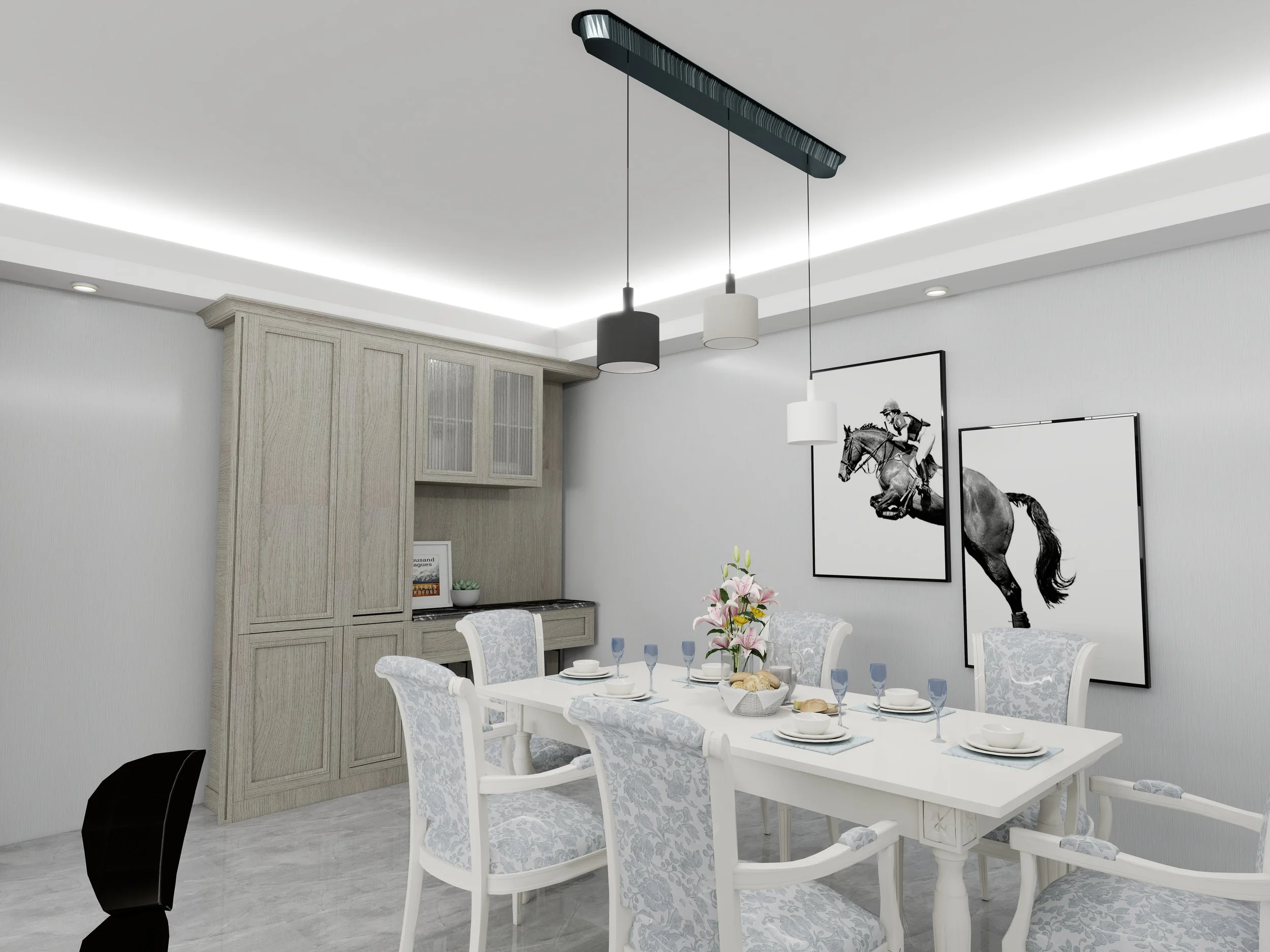 A dining room with a white table set for a meal, surrounded by upholstered chairs with a light blue and white pattern. A hanging pendant light fixture is above the table. The wall features two black-and-white horse racing photos, and a wooden cabinet is in the corner. A flower arrangement and breakfast items are on the table.