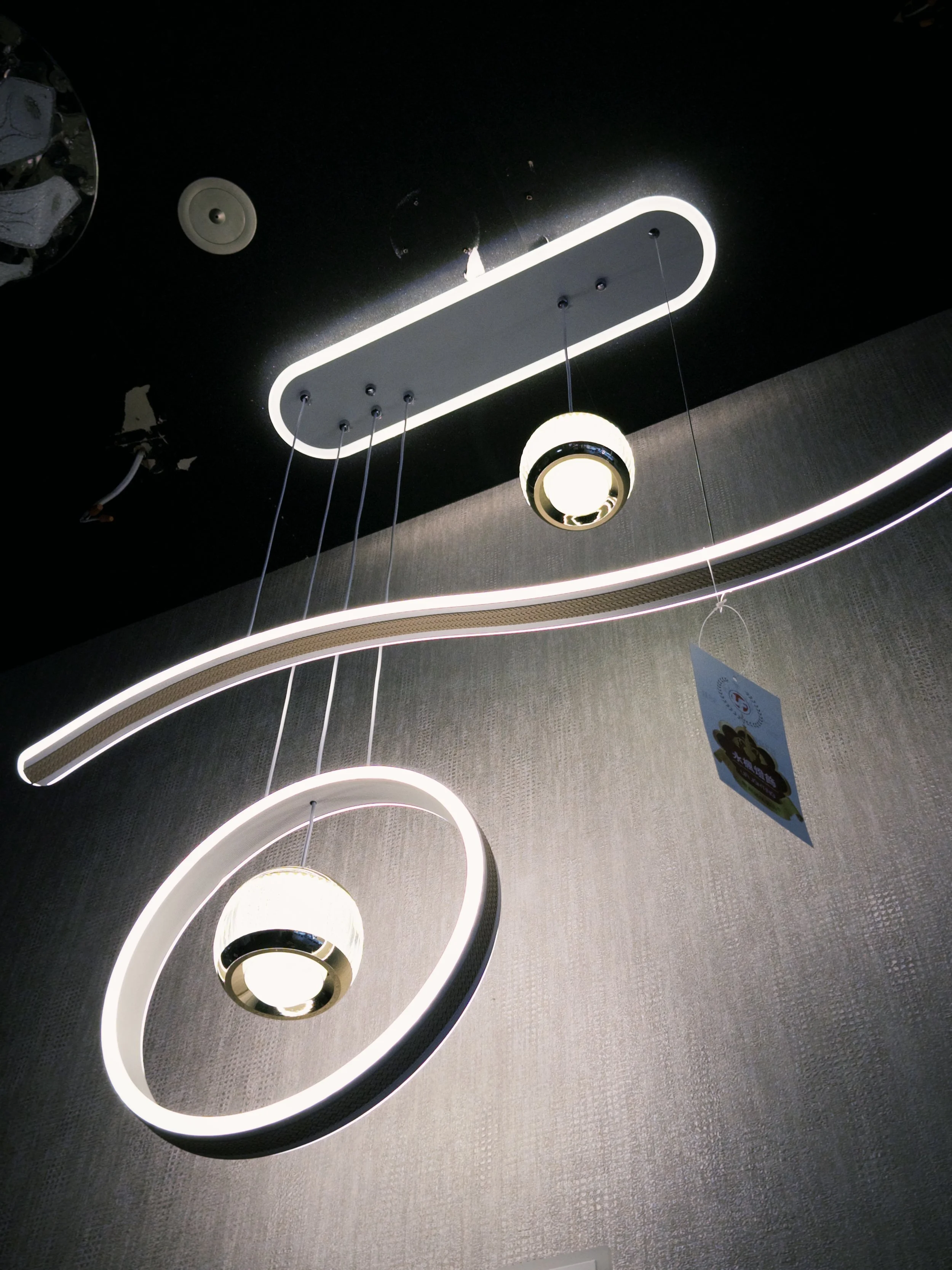 Modern ceiling lights with circular and elongated LED fixtures hanging from a dark ceiling.