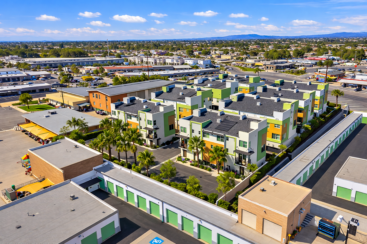 Colorful apartment complex with green, orange, and white facades, surrounded by trees and parking lots in a suburban area on a sunny day.