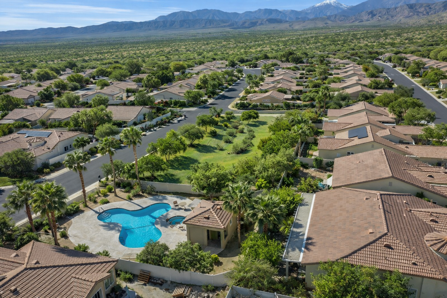 Aerial view of a suburban neighborhood with houses, trees, a swimming pool, and mountains in the background.