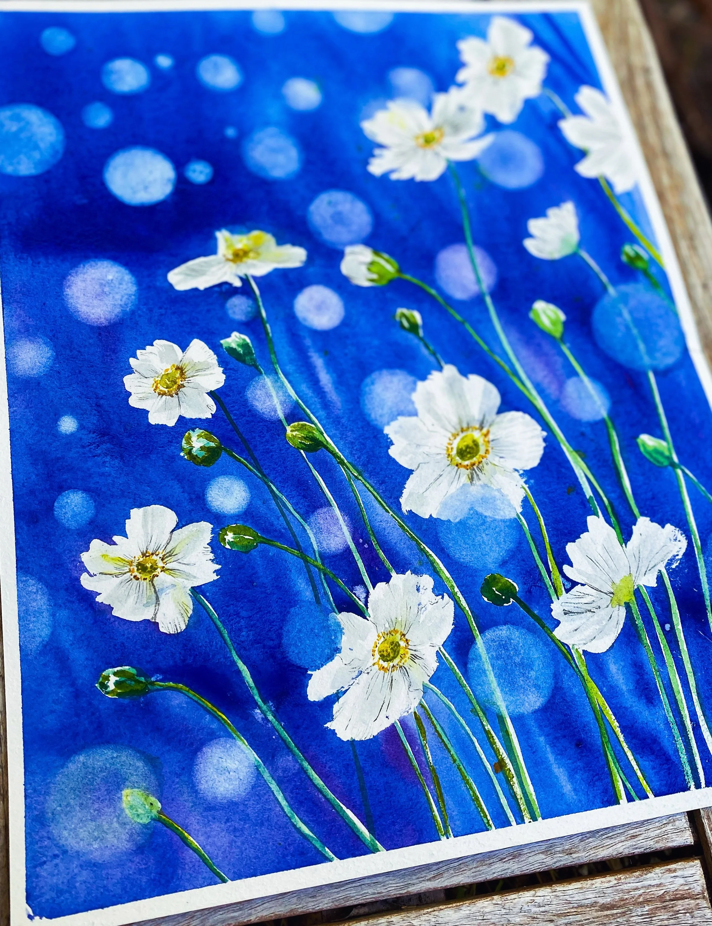 A watercolor painting of white flowers with yellow centers and green stems on a blue background with bokeh effect.