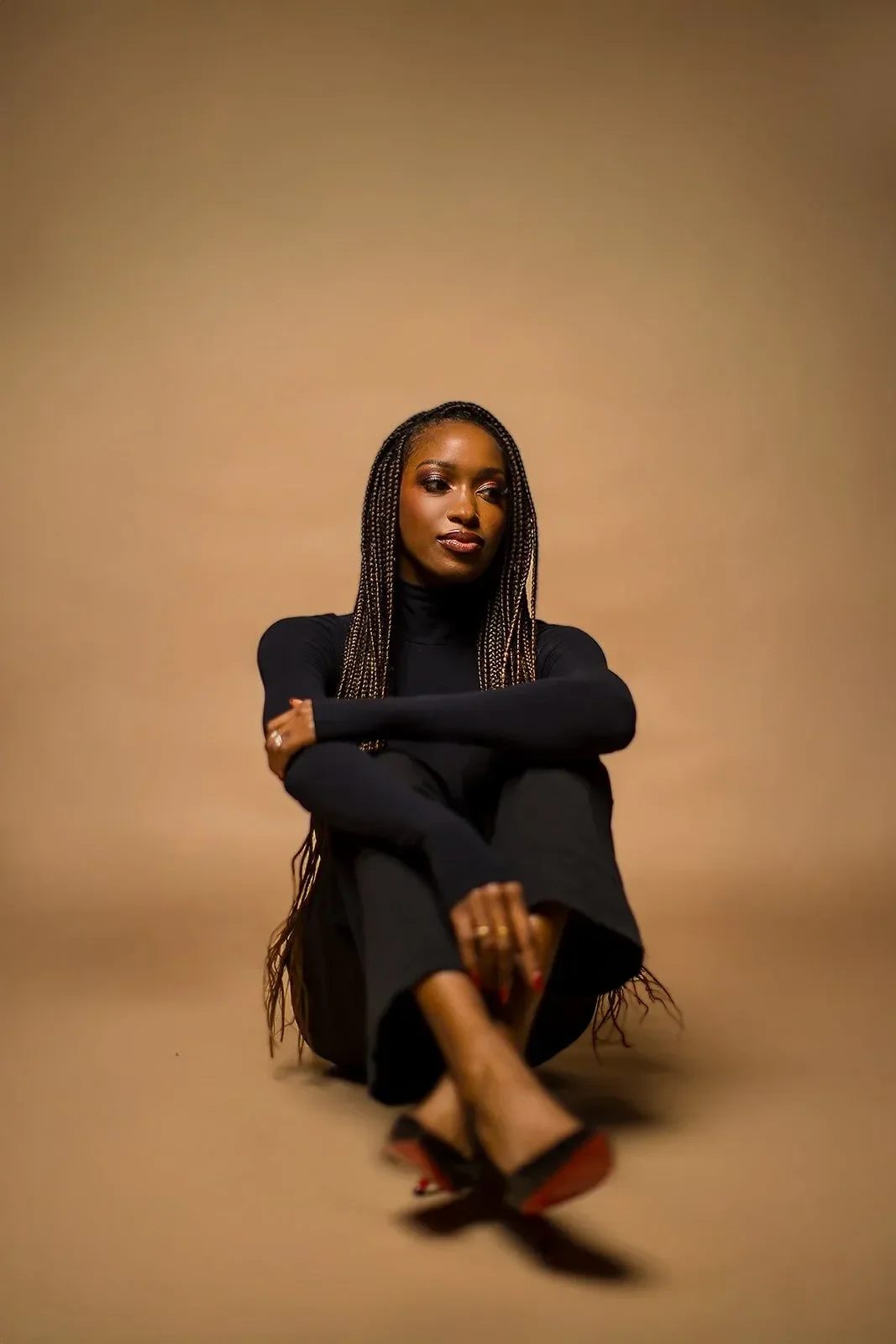 Dr. Spence sitting on the floor against a beige background, wearing a black turtleneck and black pants.