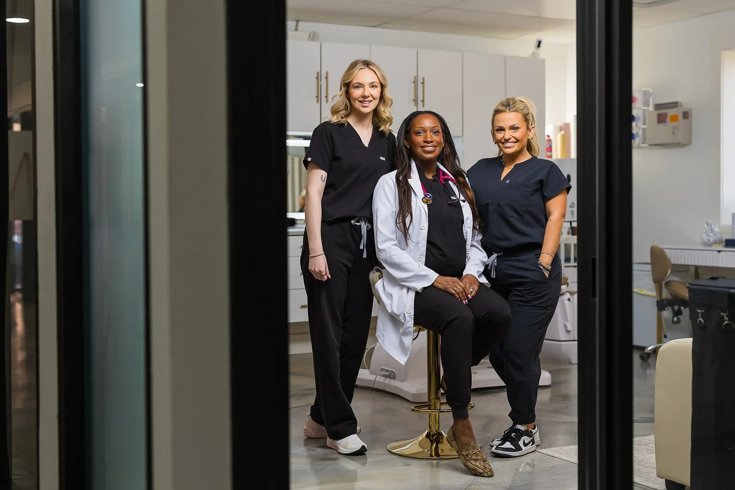 Dr. Spence in white lab coat and team in medical scrubs pose together in a medical office, smiling for the camera.