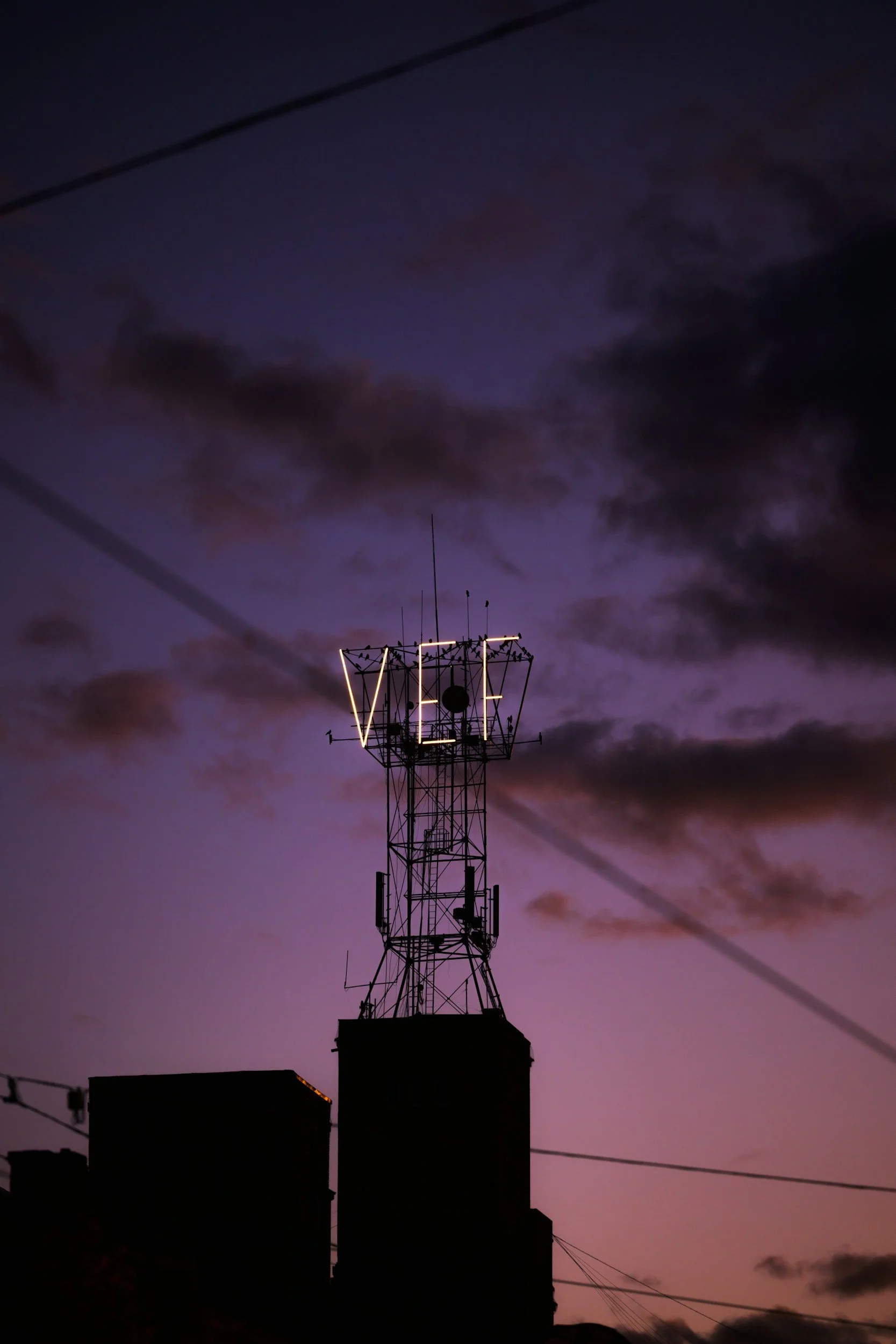 The silhouette of a communication tower against a purple and pink twilight sky with dark clouds.