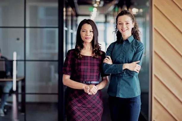 Two women standing in an office hallway, smiling.