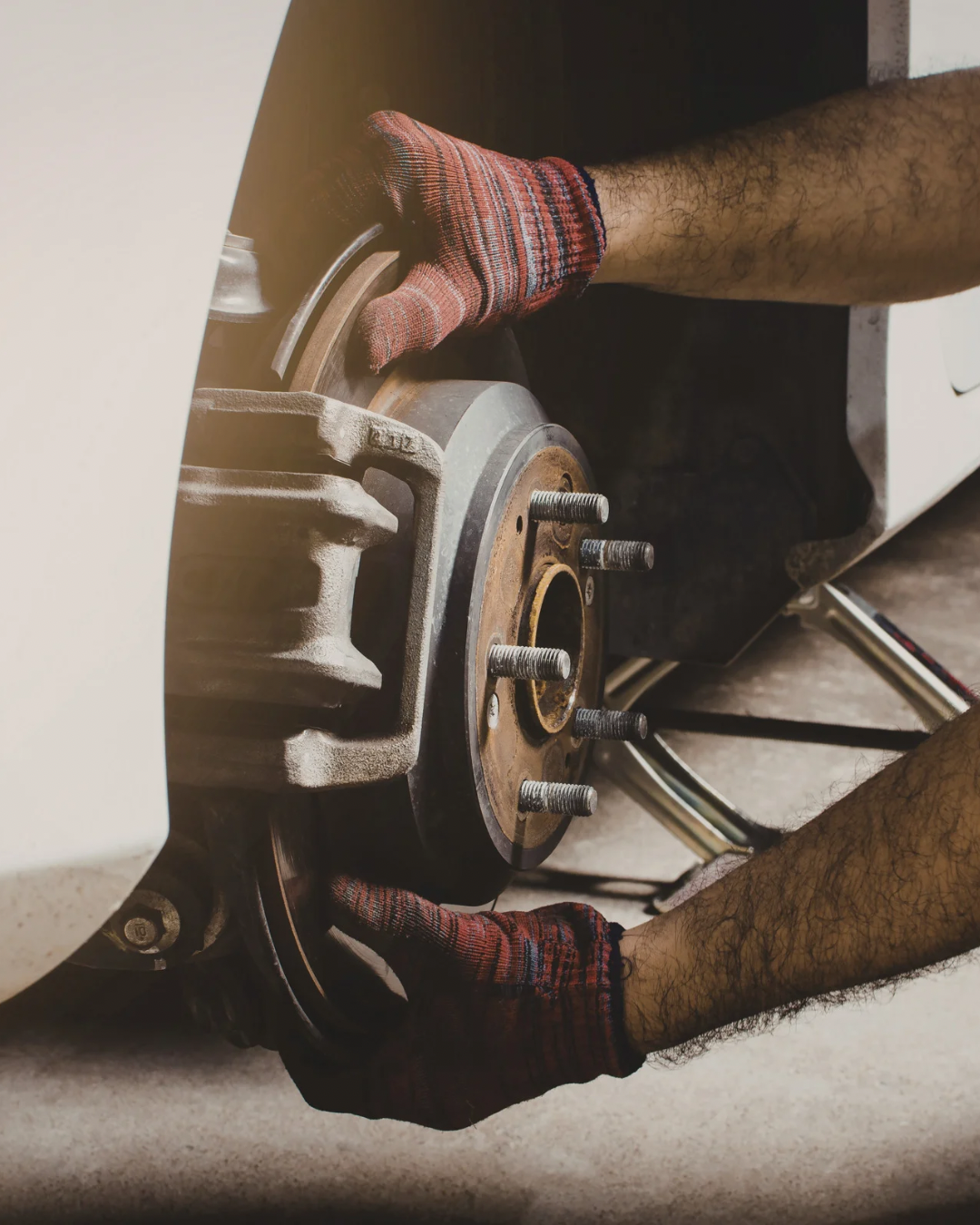 Mechanic replacing or repairing a car's brake rotor and hub assembly, wearing a striped glove, working on a white vehicle.