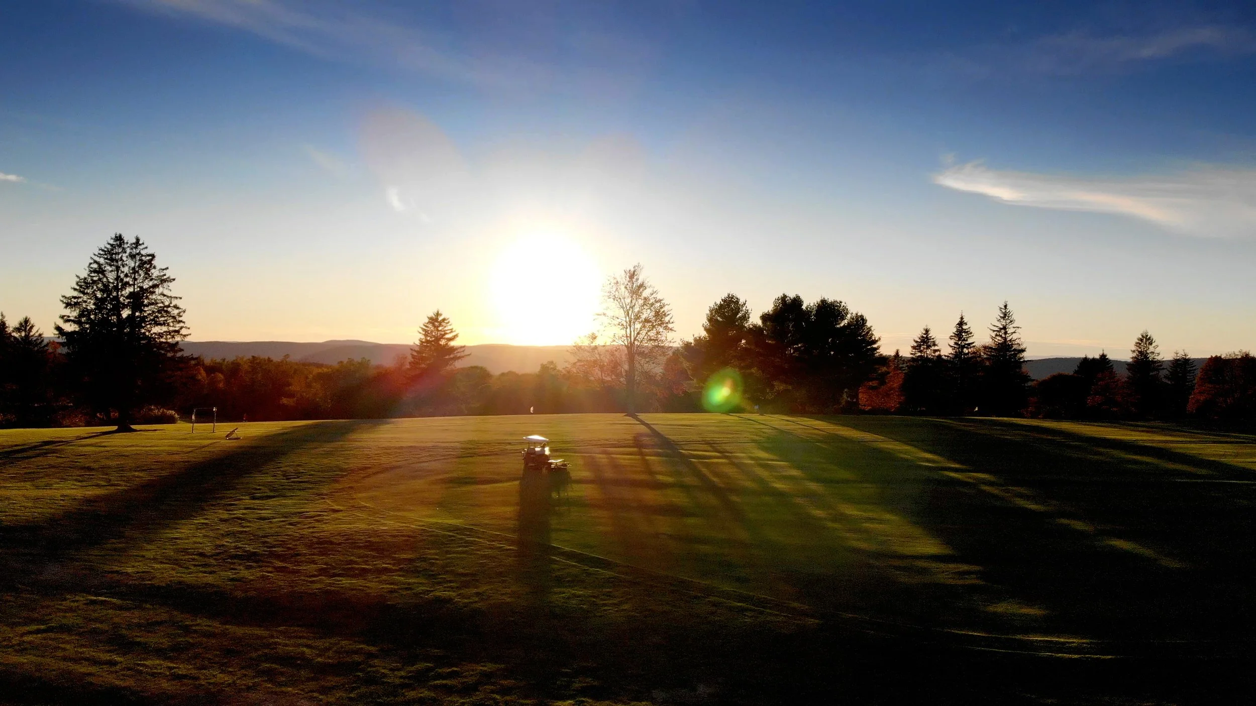 A golf course at sunset with trees in the background and a golf cart in the foreground.