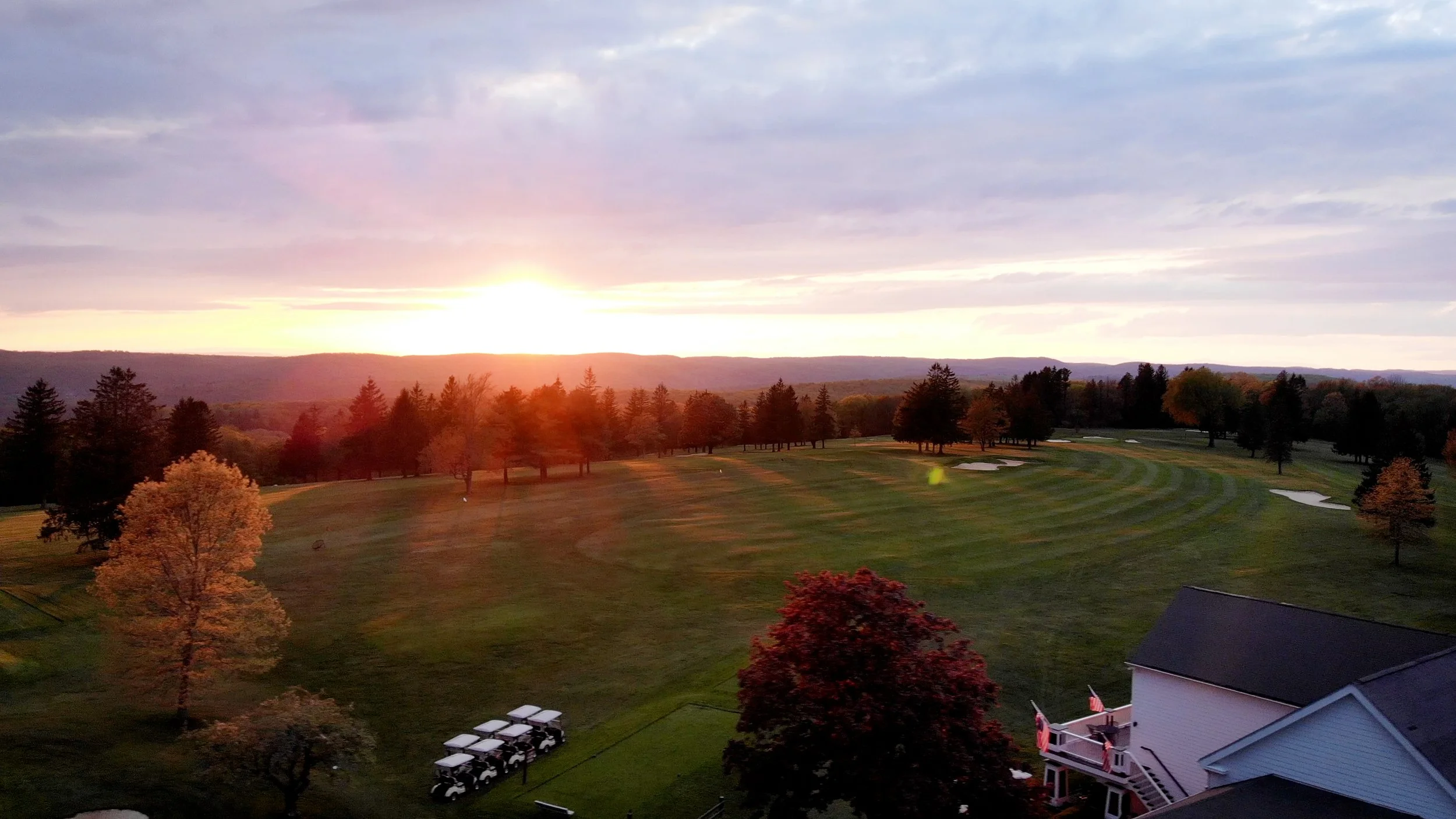 Sunset over a golf course with trees, sand traps, and a nearby house with a deck.
