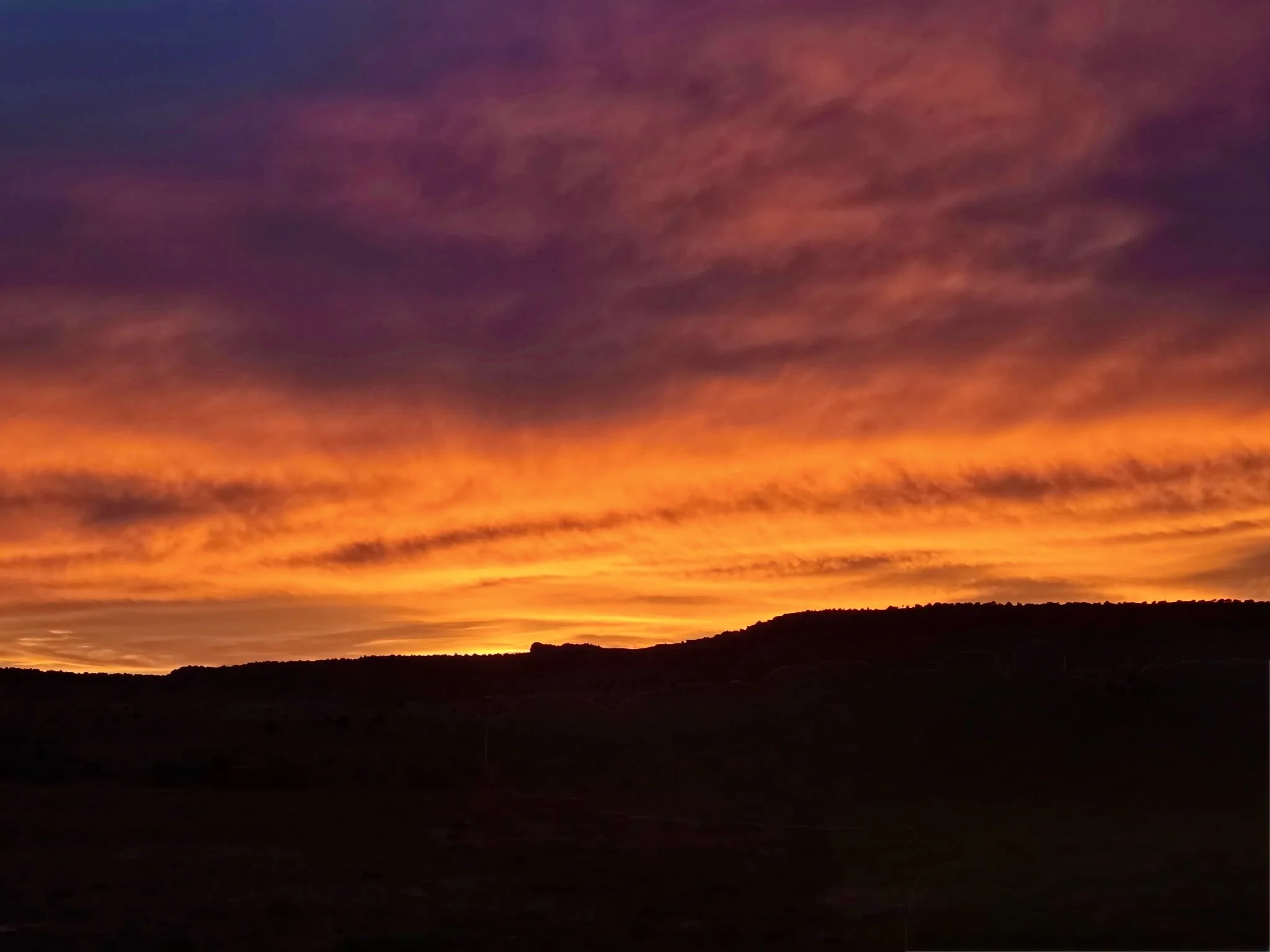 A colorful sunset over dark rolling hills, representing the beauty and uncertainty of life transitions and new beginnings at Lotus Flower Counseling