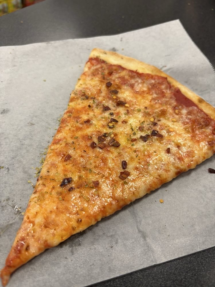 A slice of cheese pizza with herbs and crushed red pepper flakes on top, resting on a piece of parchment paper.