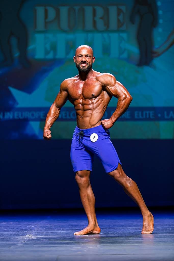 A muscular man in blue shorts posing on stage at a bodybuilding competition.