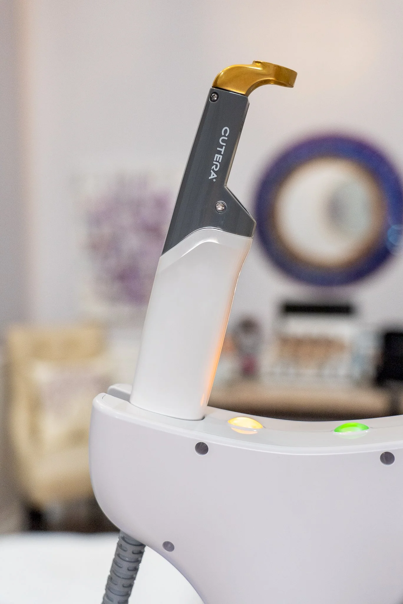 Close-up of a dental curing light with a gray handle and gold tip placed on a white dental handpiece holder, with blurred dental equipment in the background.