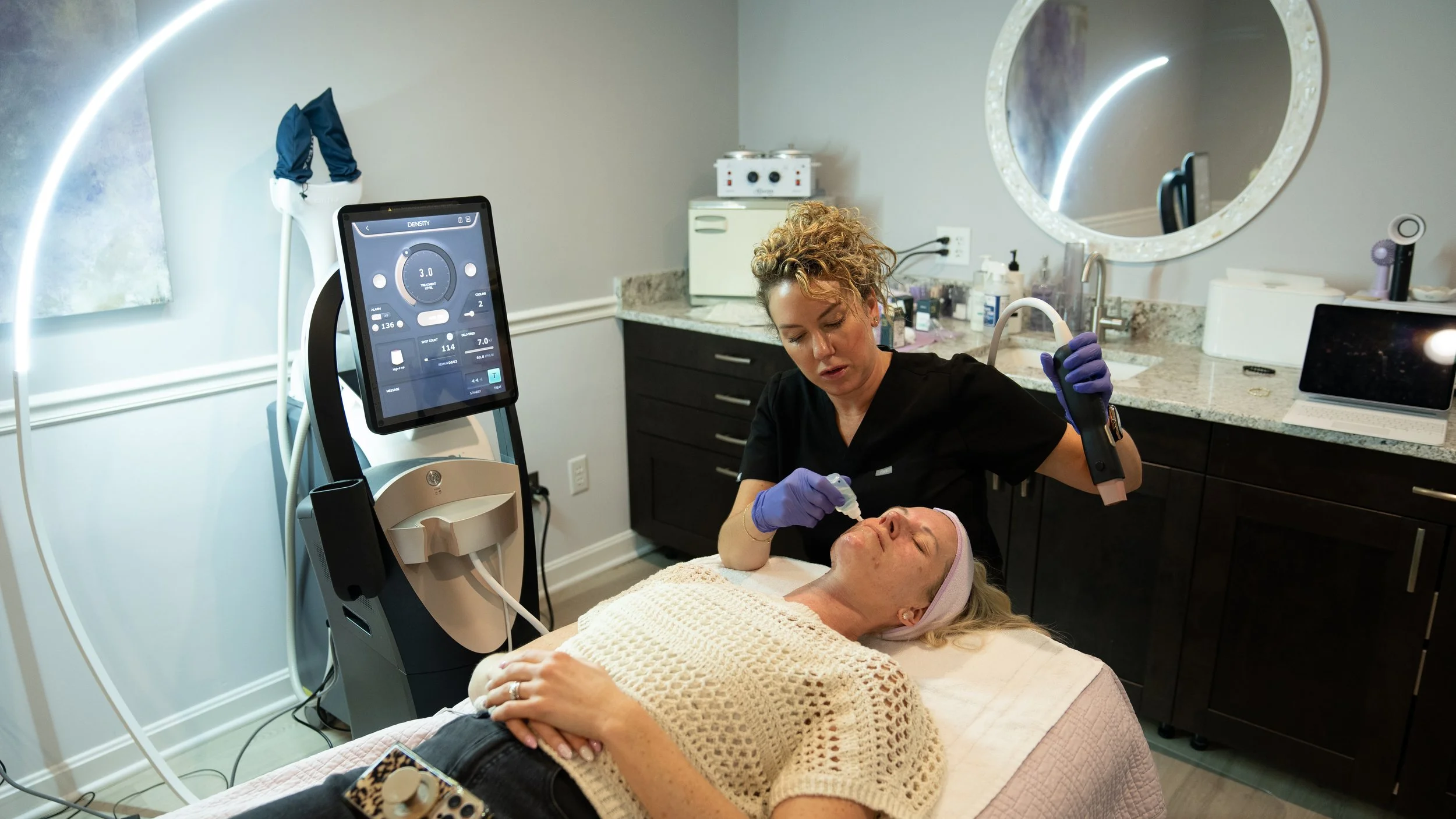A woman receiving a facial treatment in a spa or medical setting with a healthcare professional using a laser device.