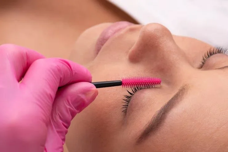 A person receiving eyelash extension application with a glue wand in a beauty salon.