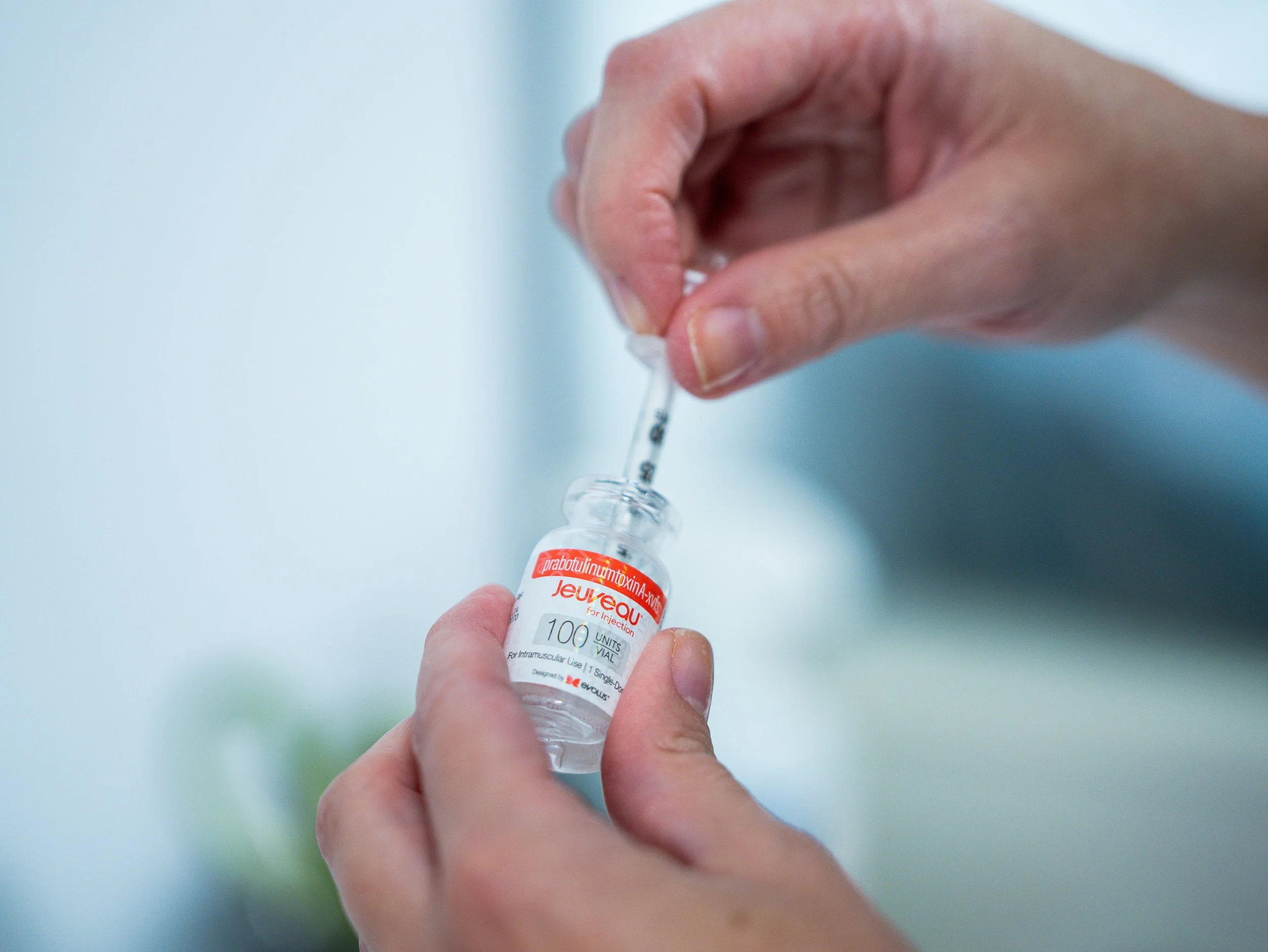 A person’s hand holding a small glass vial labeled with a medical medication name and dosage, with a dropper above it.