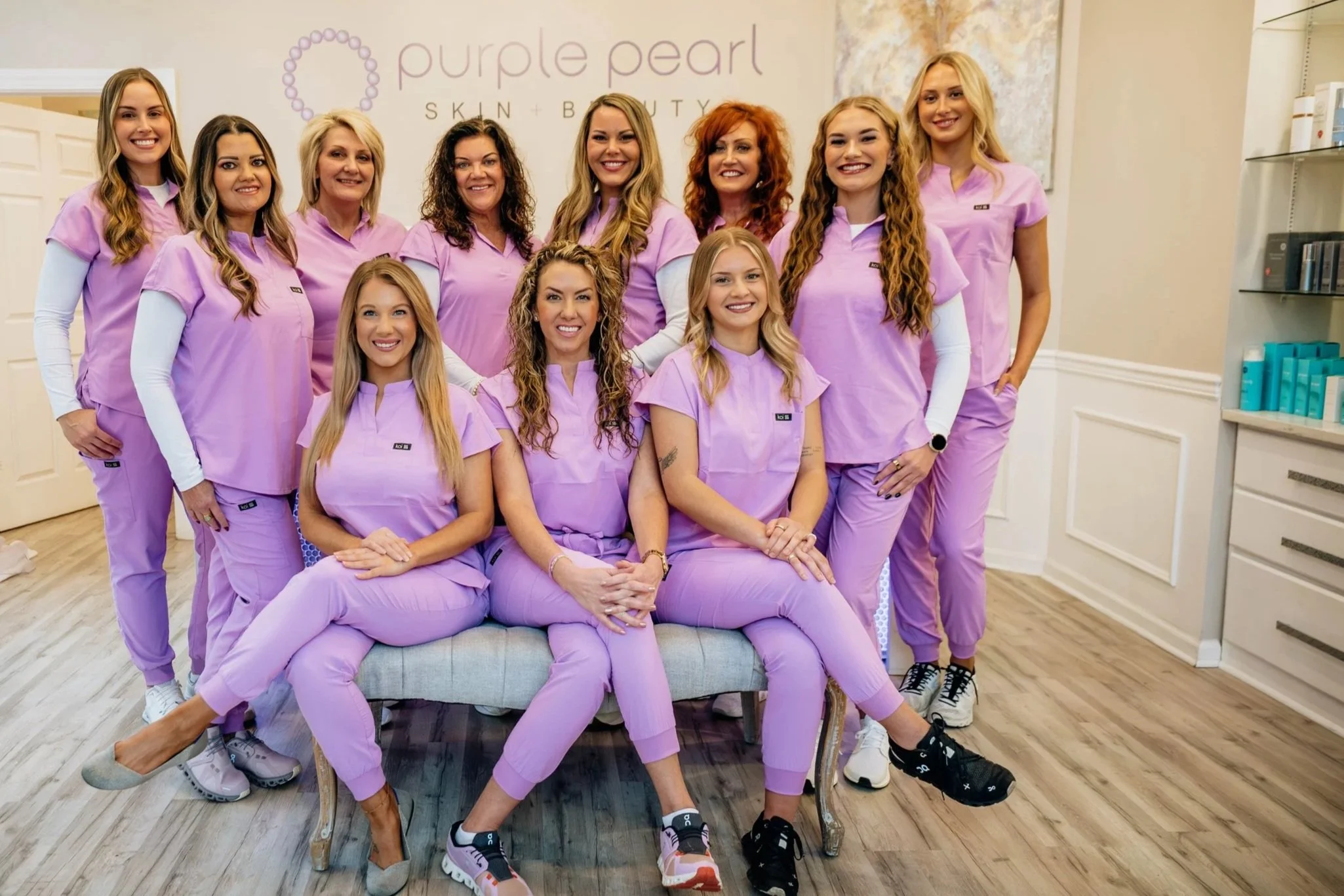 Group of women in matching purple scrubs posing in a skin and beauty clinic.