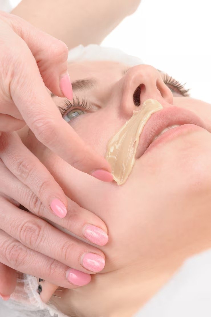 A woman receiving facial treatment with a skincare mask being applied to her upper lip area.