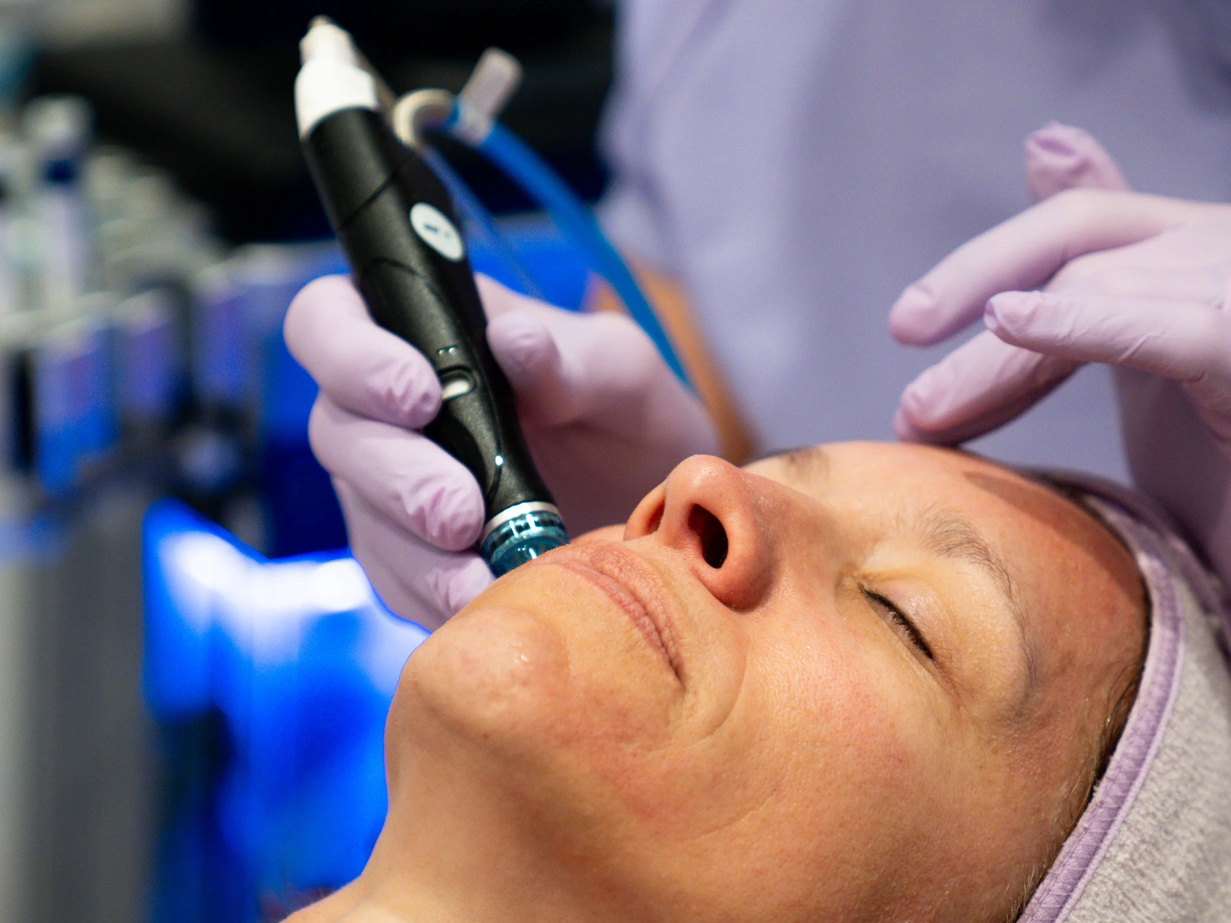 A person receiving a cosmetic or medical treatment with a device applied to their face, while lying down with eyes closed.