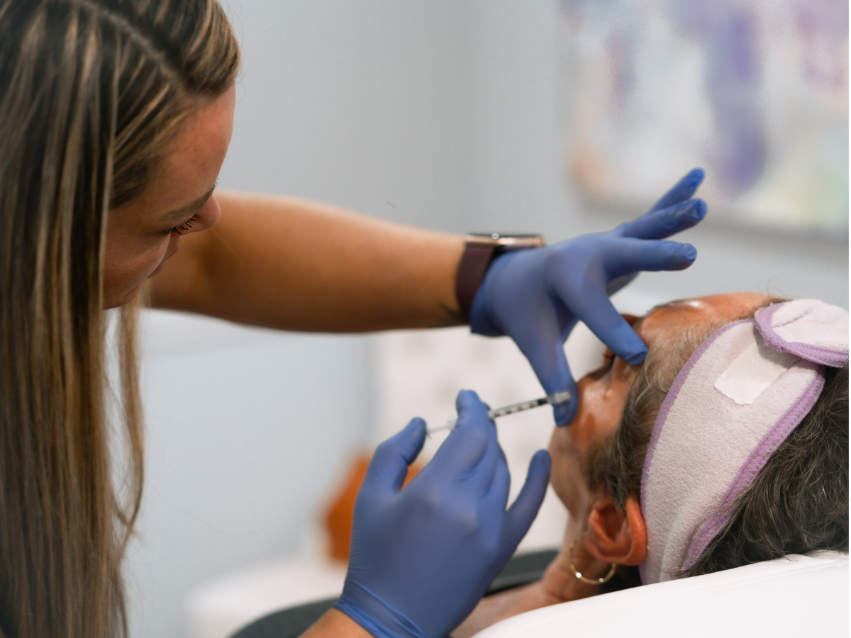 A woman receiving a facial injection from a healthcare professional wearing blue gloves.