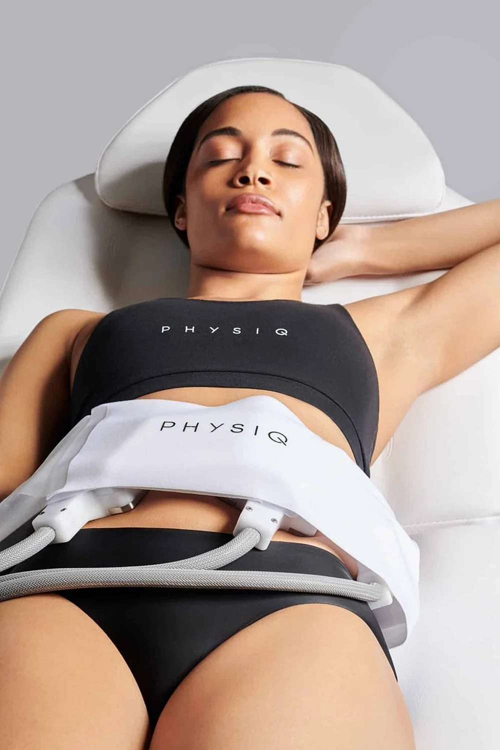 A woman lying on a treatment table with a medical device on her abdomen, appearing relaxed with her eyes closed.