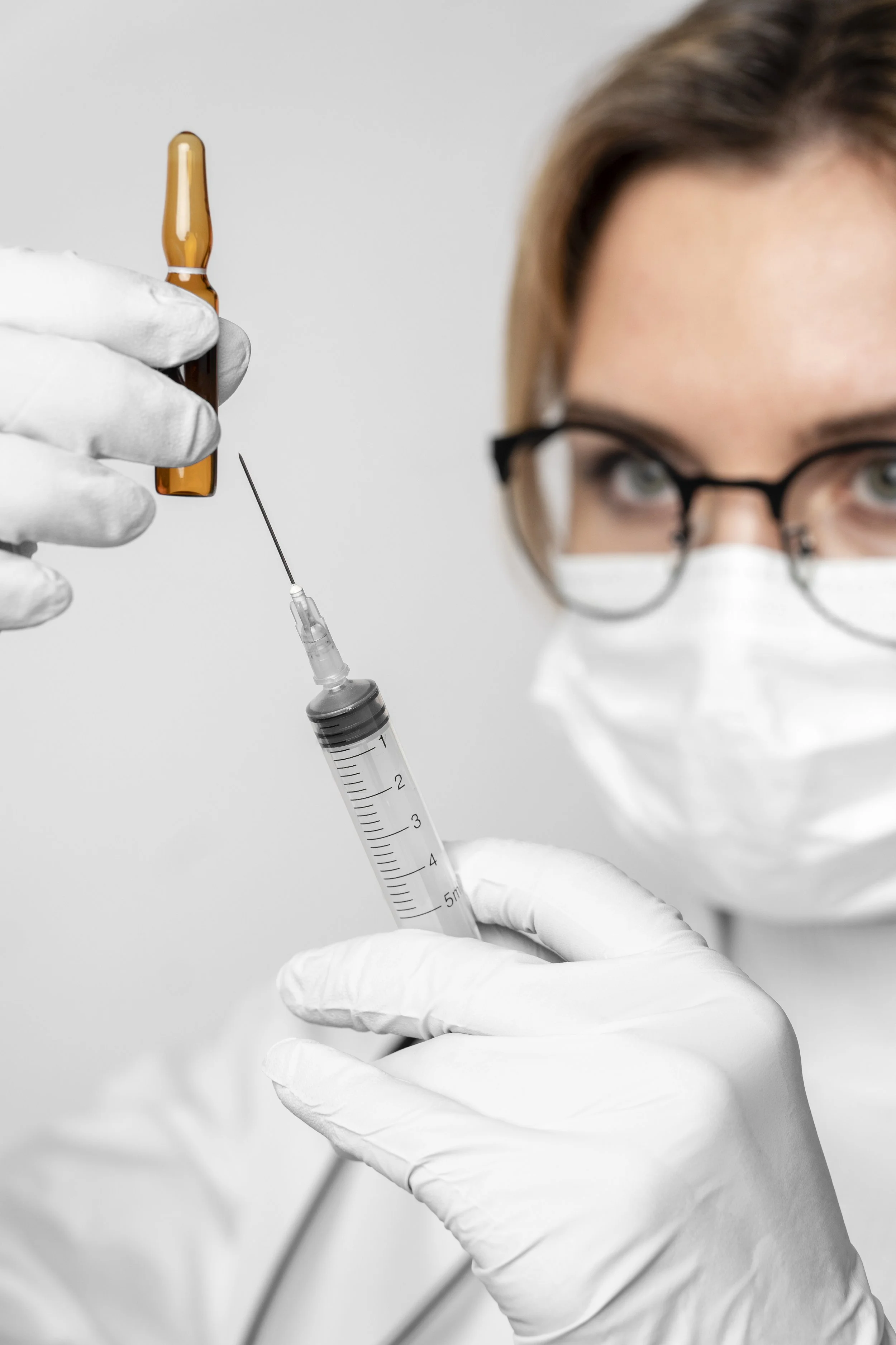 Medical professional wearing white gloves and a face mask preparing a syringe with a vaccine or medication.