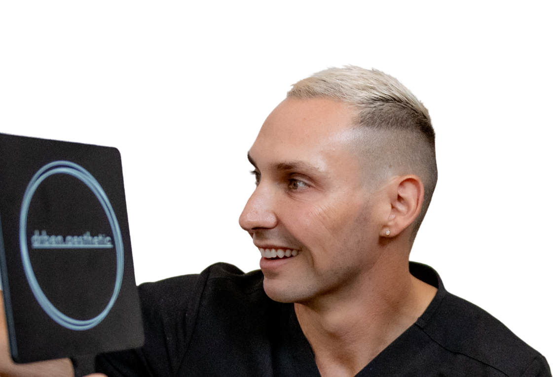 A person with short, bleached hair smiling and holding a tablet with a circular design on the screen.