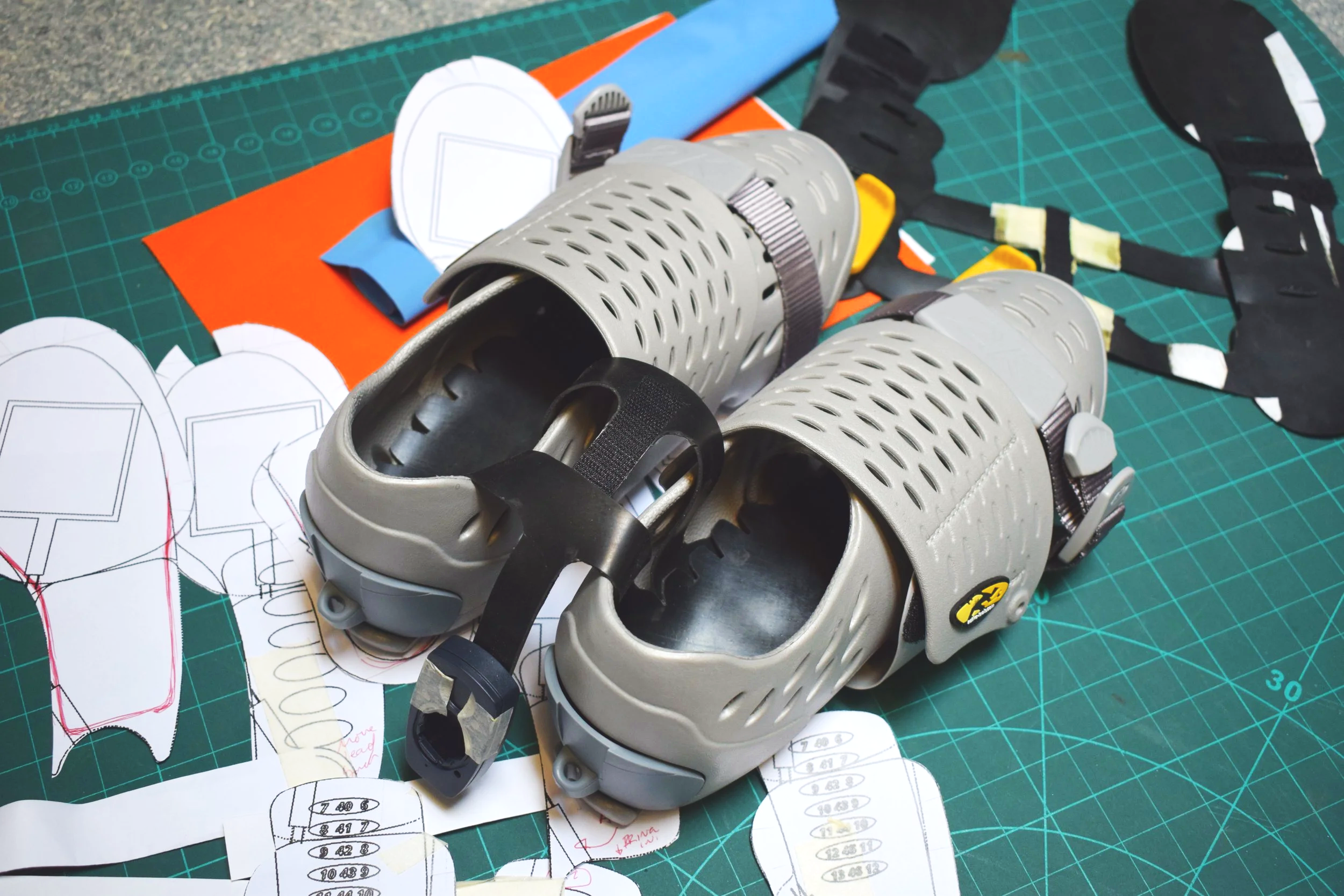 A pair of grey rowing shoes rescue boots placed on a green cutting mat with paper templates and sketches nearby.