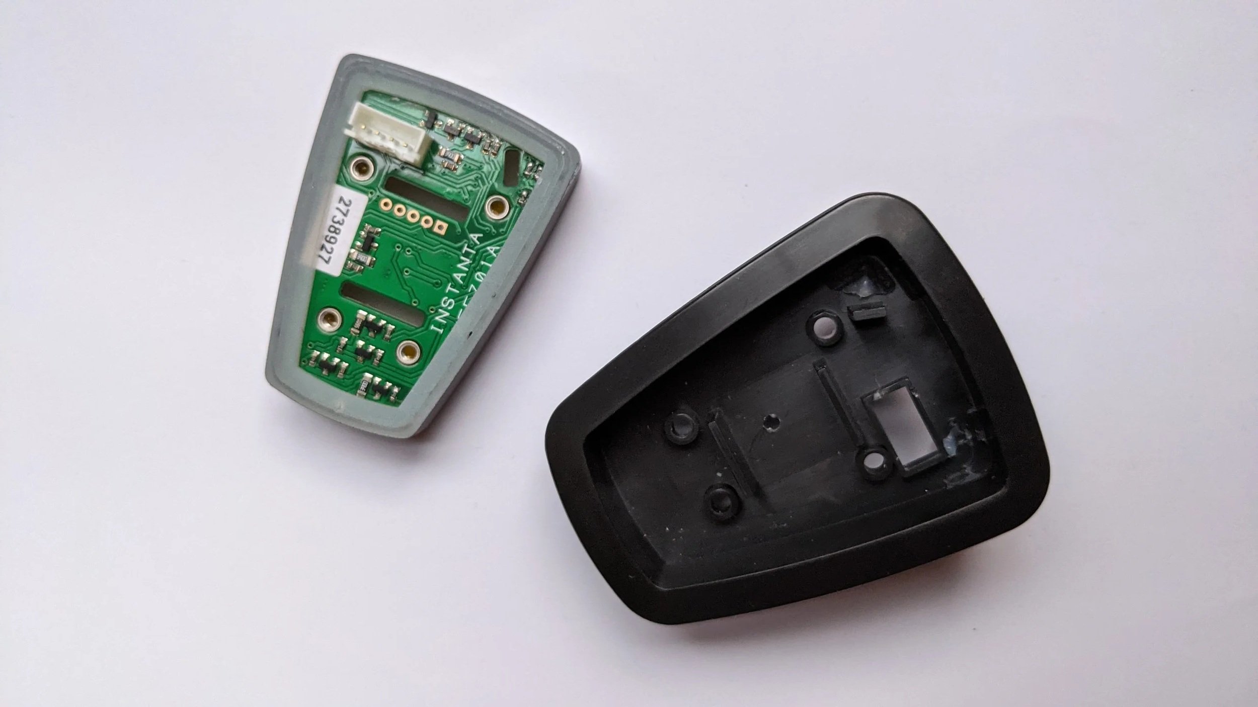 Disassembled garage door remote control with circuit board and empty black casing on a white surface.