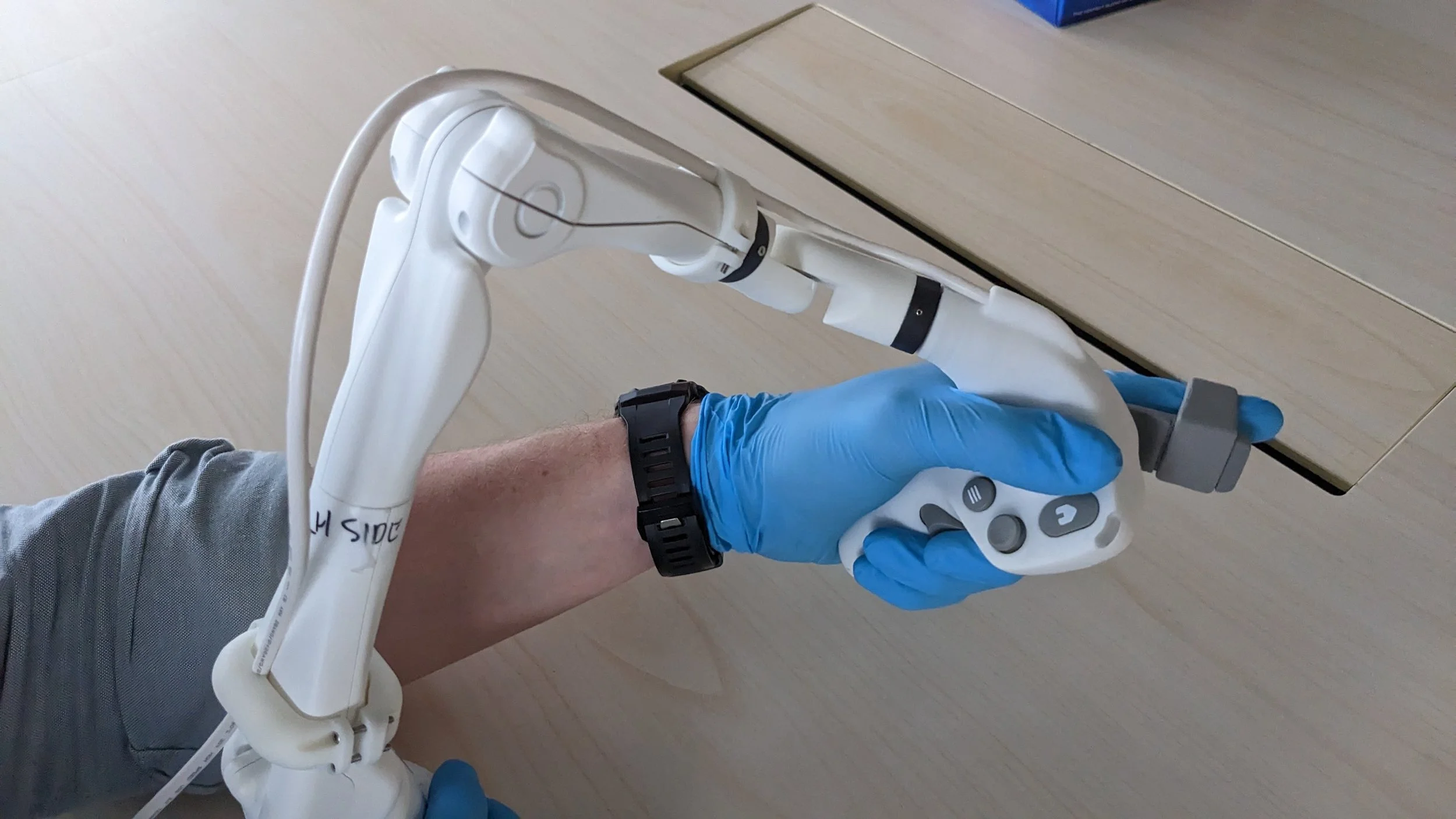 A healthcare worker wearing blue gloves holding a surgical robot input mechanism which is connected to medical equipment.