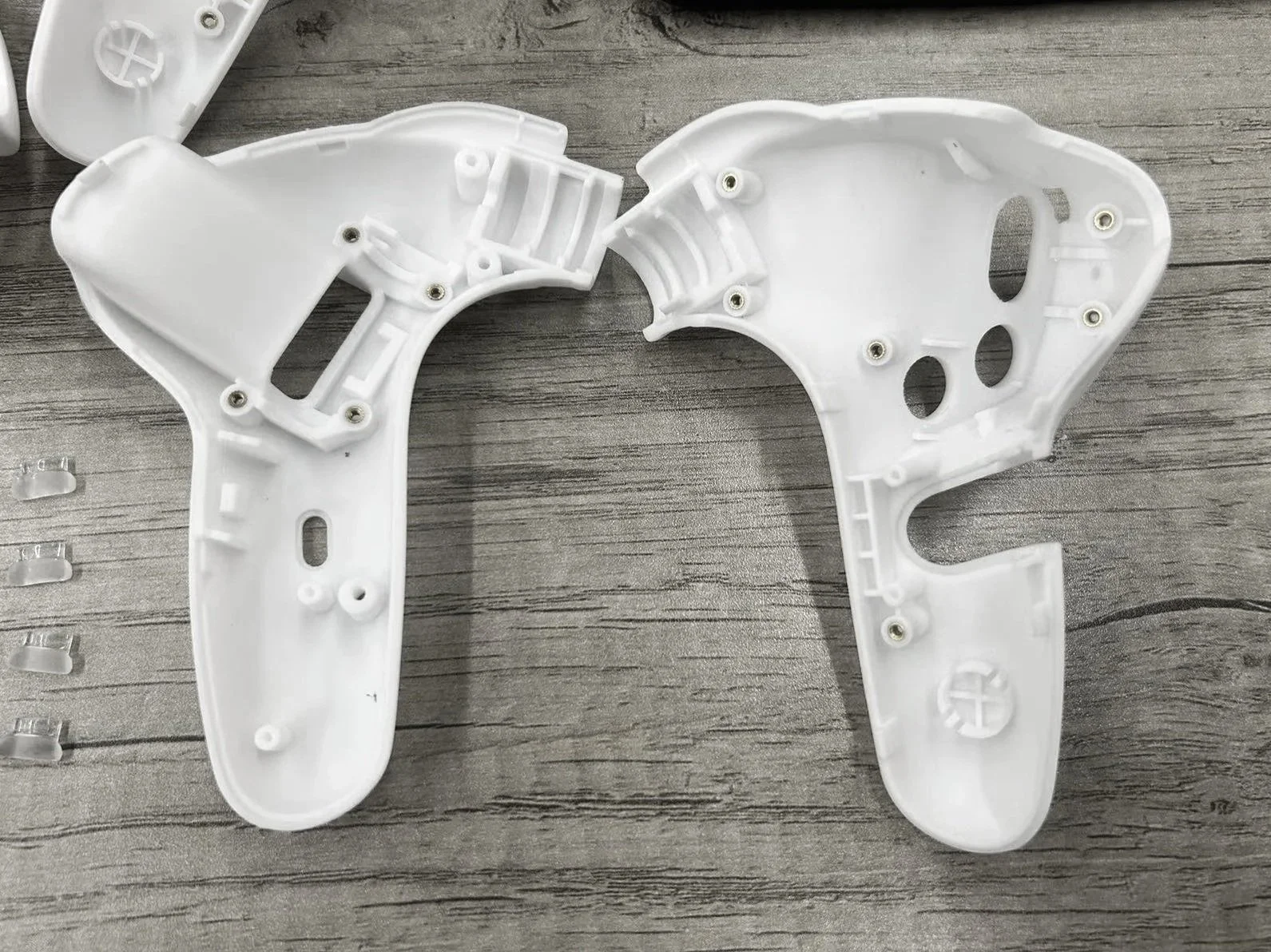 Two white plastic parts with screws attached, laid out on a wooden surface, possibly components of a device or casing.