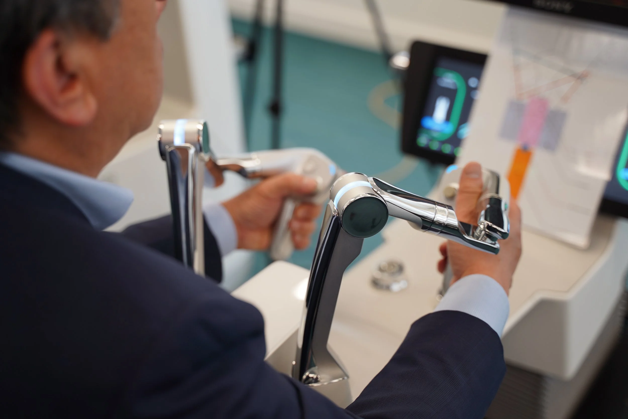 Person in a suit using a robotic prosthetic arm to operate a touchscreen device at a medical or research facility.
