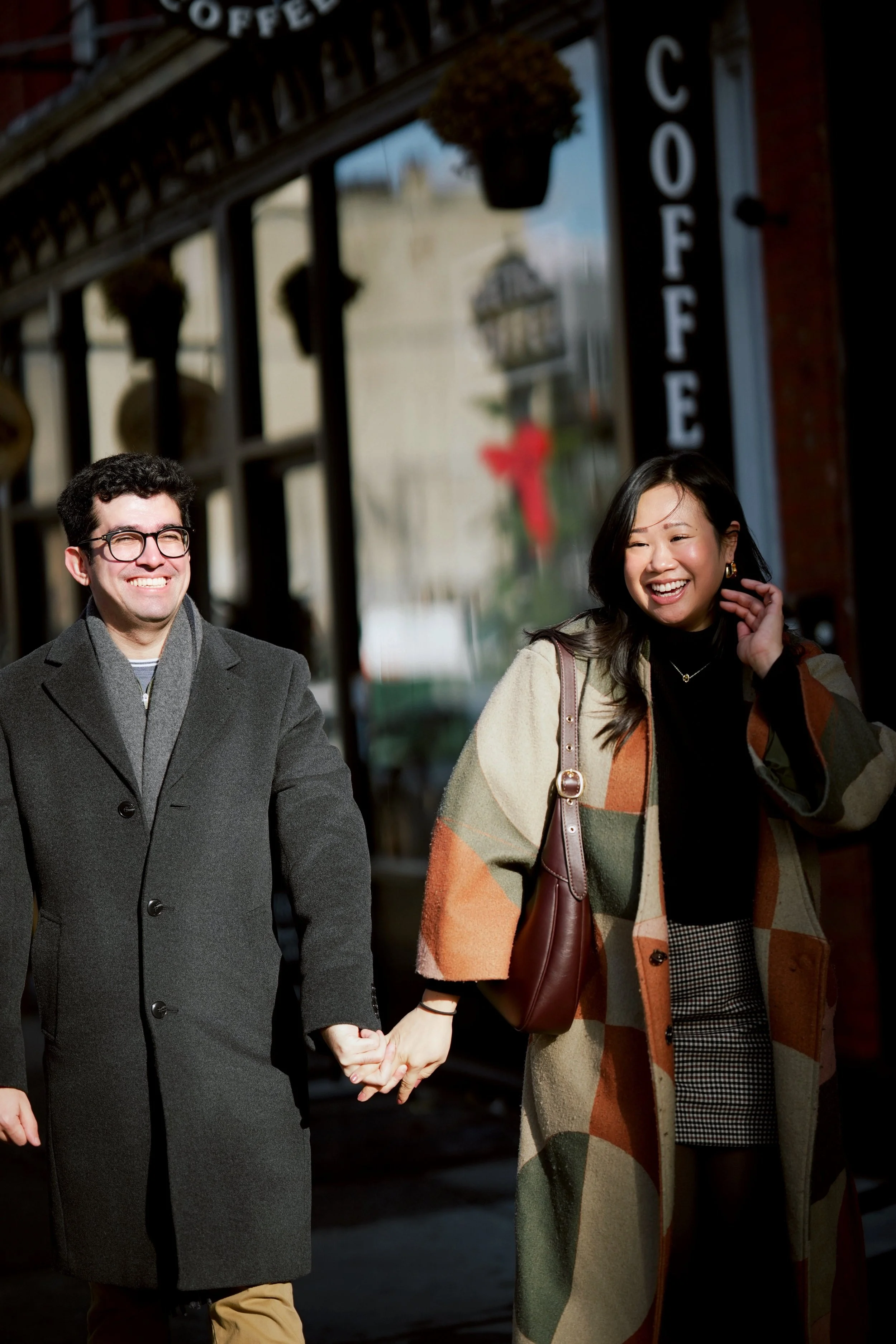 A happy couple holding hands and walking outside a coffee shop on a sunny day, smiling and enjoying each other's company.