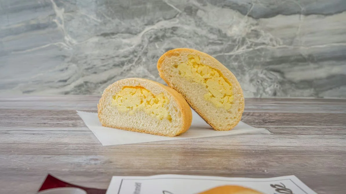 A sliced custard-filled baked good on a piece of paper on a wooden surface with a marble background.