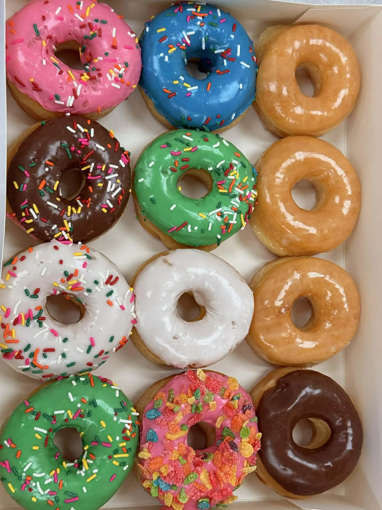 A box of twelve assorted colorful donuts with sprinkles and glaze.