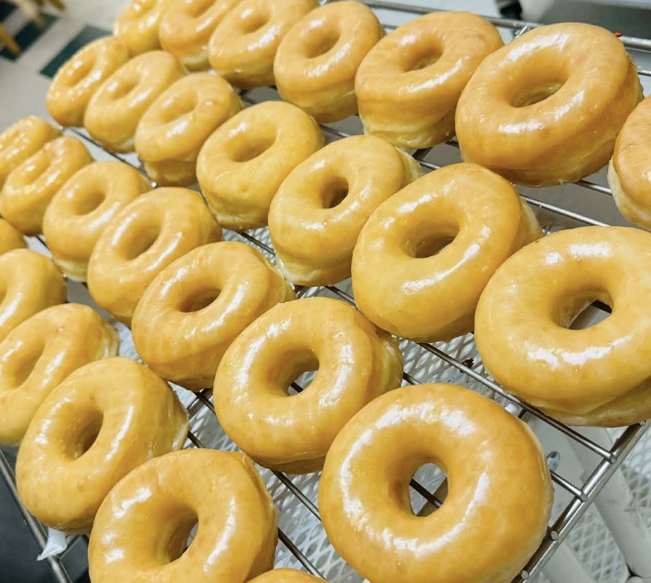A tray of glazed donuts arranged on a wire rack, with a shiny, golden-brown exterior.