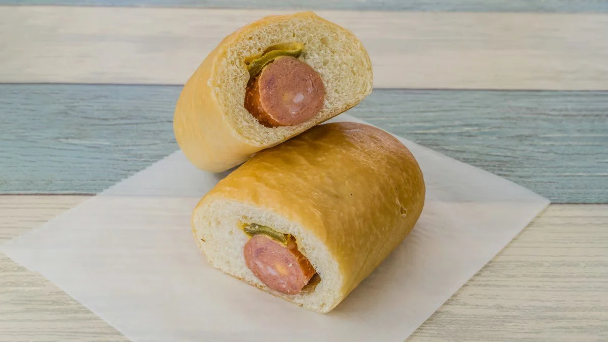Sliced hot dog buns with hot dogs and pickles inside.