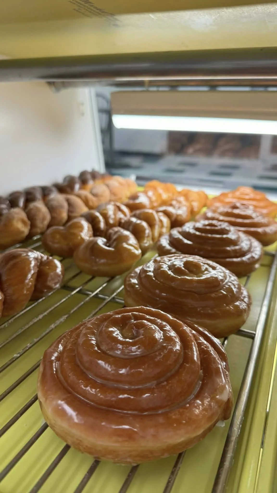 Close-up of glazed cinnamon rolls on a cooling rack in a bakery display case.