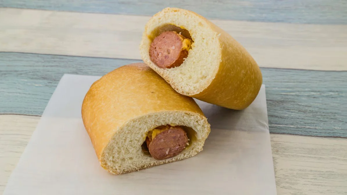 Two halved hot dog buns filled with hot dogs and mustard, placed on a white napkin on a wooden surface.