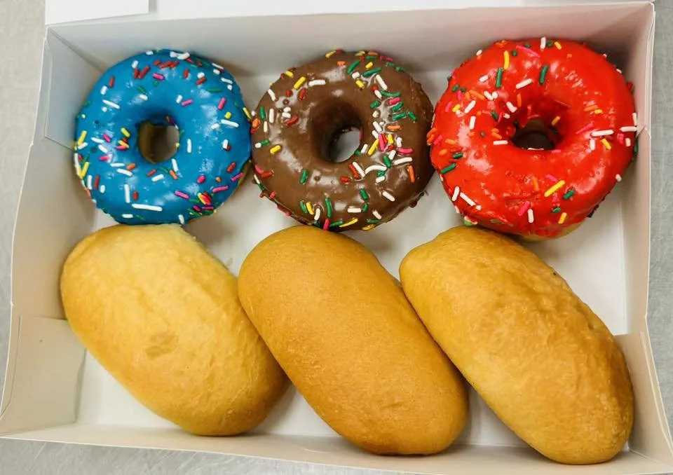 A box containing three assorted donuts with colorful sprinkles and three pineapple-shaped pastries.