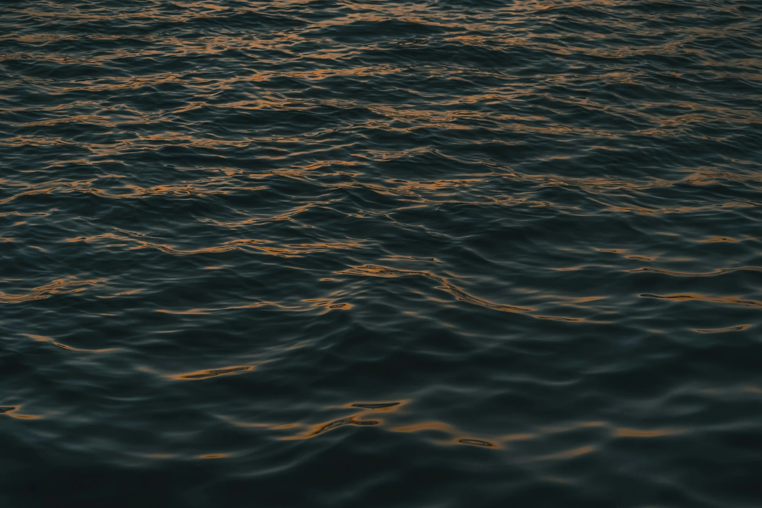 Calm ocean surface with gentle Waves reflecting a warm, orange sunset or sunrise.