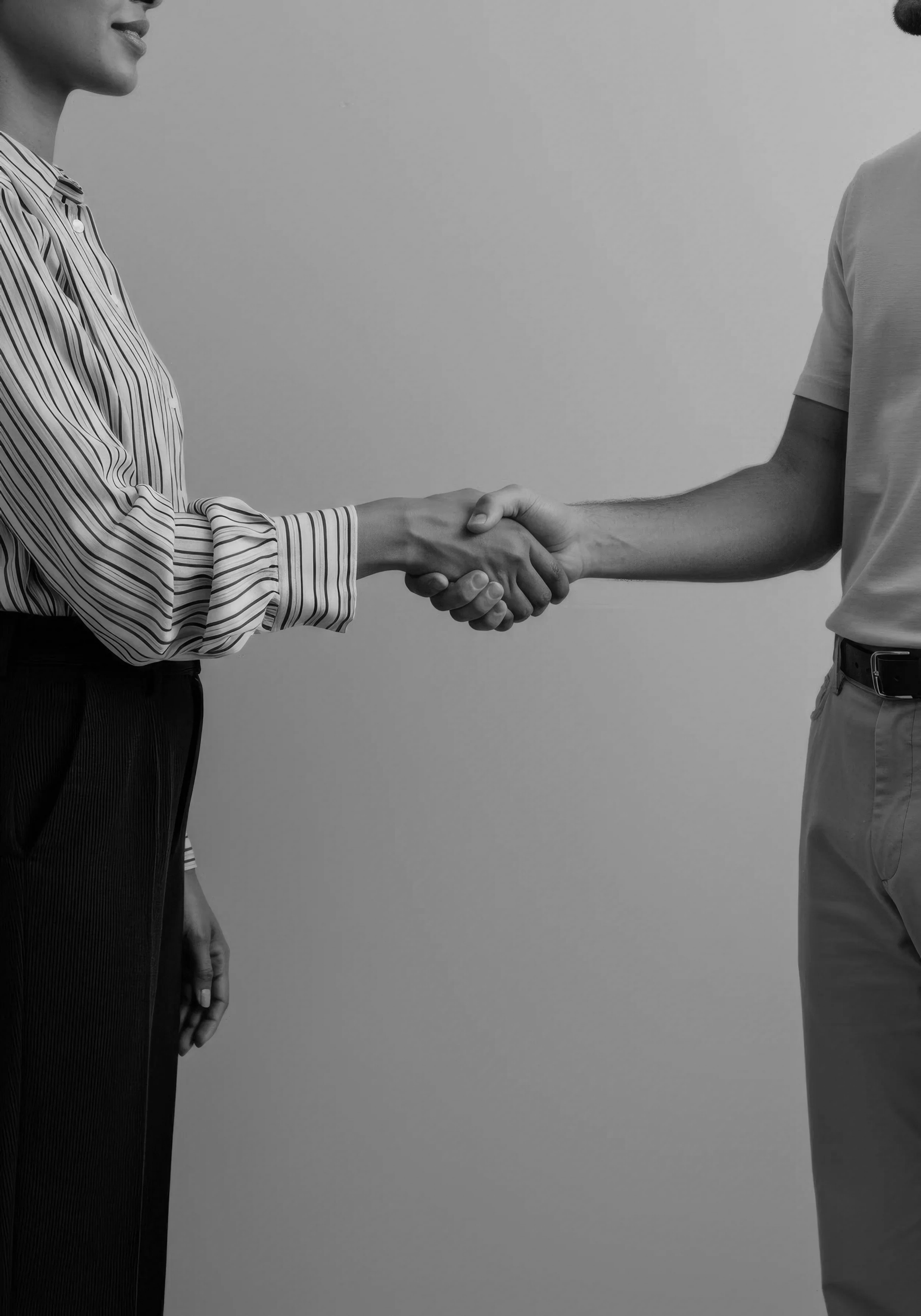 Two people shaking hands, with only their torsos and arms visible; one person wearing a striped shirt and the other wearing a plain t-shirt, against a plain background.
