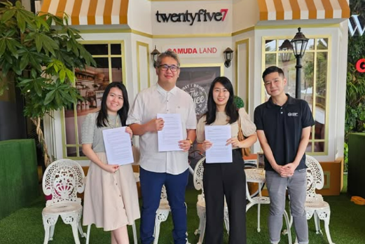 MoU of Sleepy Bear Group. Four young adults standing outside a restaurant, holding documents and smiling, with a sign that reads 'twentyfive7' and 'AMUDA LAND' behind them.