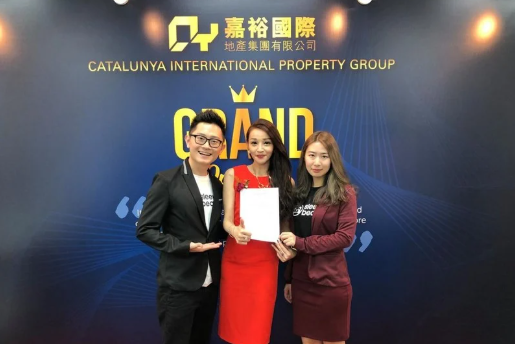 MoU of Sleepy Bear Group. Three individuals standing in front of a blue backdrop at a Catalanya International Property Group event, holding a white certificate or document.